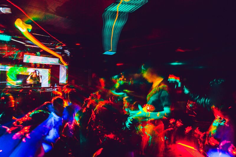 People Dancing in Nightclub and Young Woman DJ Performing.