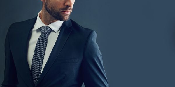 Man in a sharp black suit and patterned tie looking to the side.