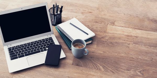 A tidy workspace with a laptop, smartphone, notebooks, pen, cup of coffee, and pens holder.