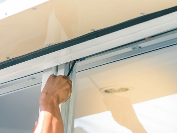 Person using a screwdriver to fix a window frame.