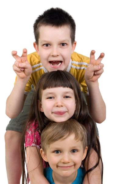 Three playful children stacked up, smiling and making faces.