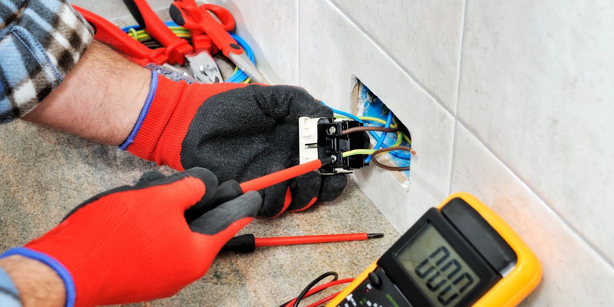 Electrician working on wiring with tools and multimeter.