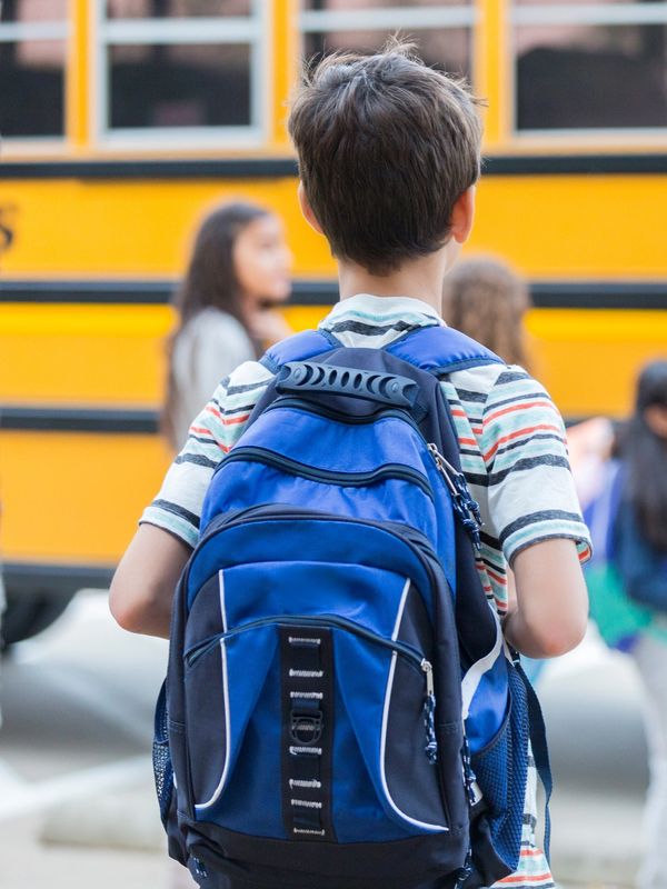 Boy with a blue backpack waiting near a school bus.