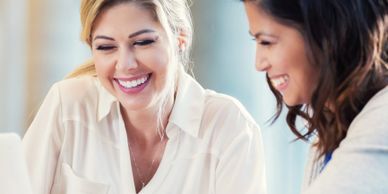Two women smiling and working together on a laptop.