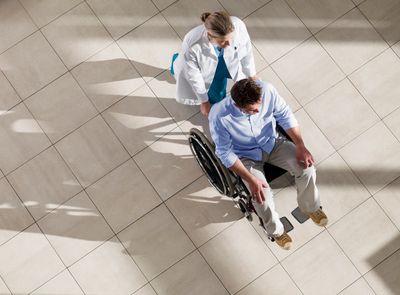 Healthcare professional assisting a man in a wheelchair in a bright hallway.