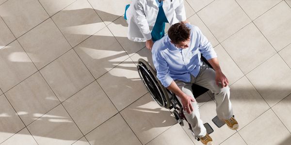 Healthcare professional assisting a man in a wheelchair in a bright hallway.