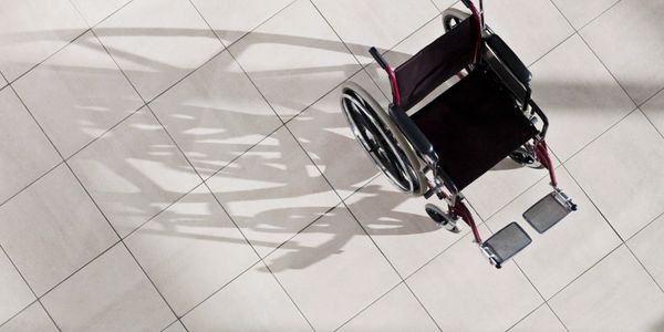 Empty wheelchair casting a shadow on tiled floor.