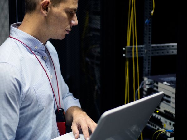 Technician working on network servers with a laptop in a data center.