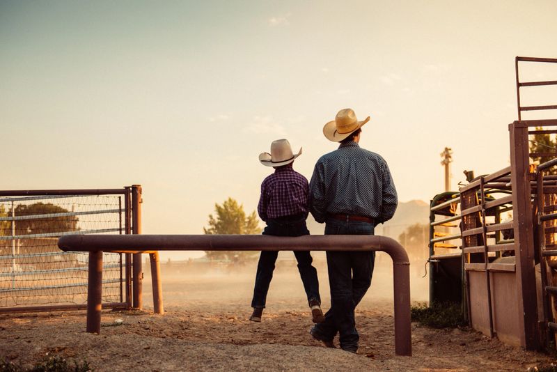 Father and son sitting by rodeo arena at sunrise