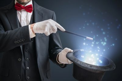 Magician in tuxedo performing a magic trick with glowing sparkles.