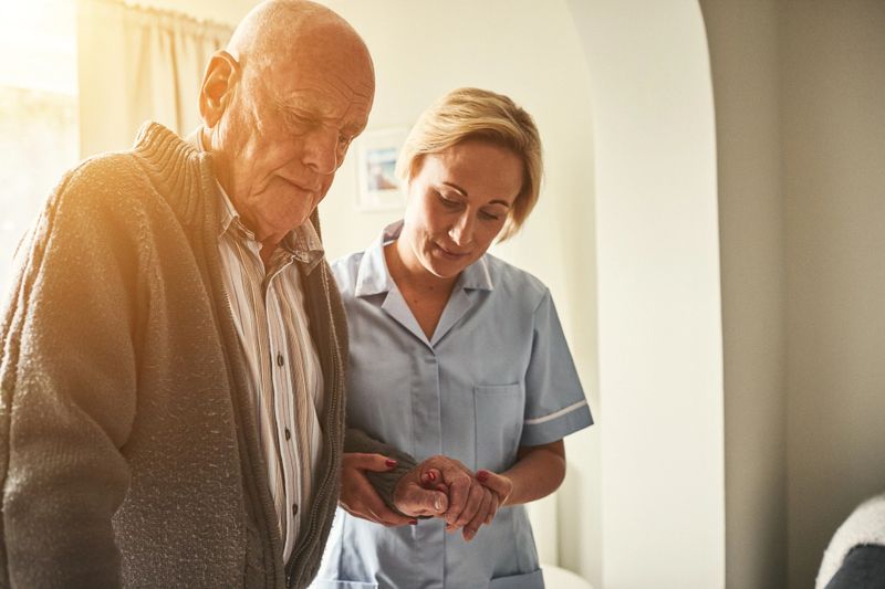 Female carer helping patient to walk at home. Home caregiver supporting senior man while walking.