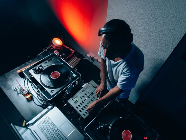 DJ mixing music with turntables and laptop in a dimly lit room.
