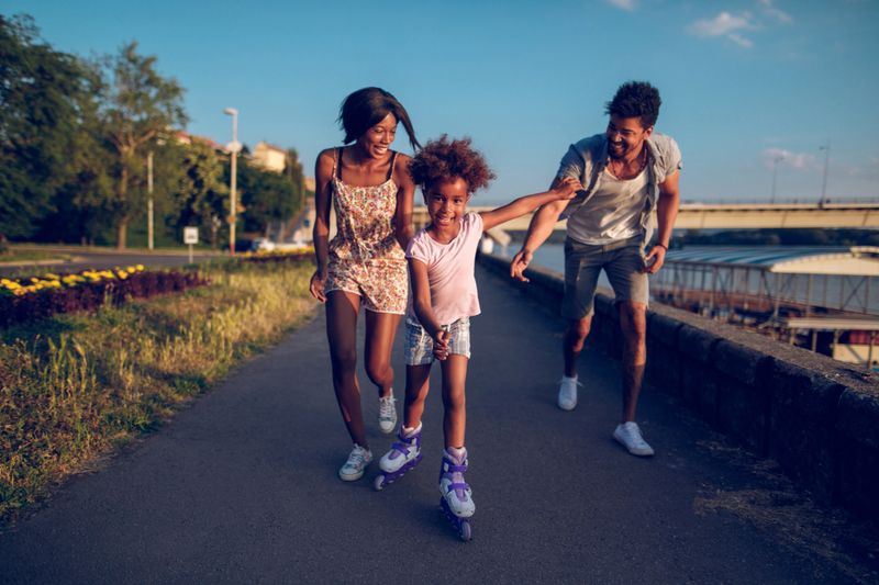 Parents assisting their daughter while roller skating at sunset.