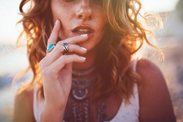 A woman with curly hair and rings touching her lips.