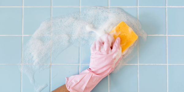 Hand cleaning tiles with sponge and soap bubbles.