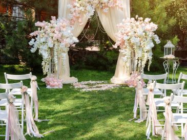 Outdoor wedding arch decorated with flowers and white chairs.