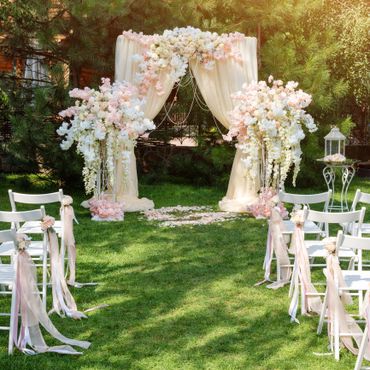 Outdoor wedding setup with floral arch and decorated chairs.