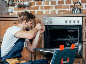 Technician repairing a kitchen oven in a rustic setting.