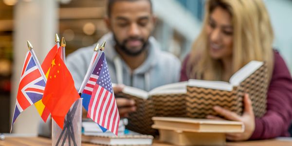 Small international flags on a table with two people studying in the background.