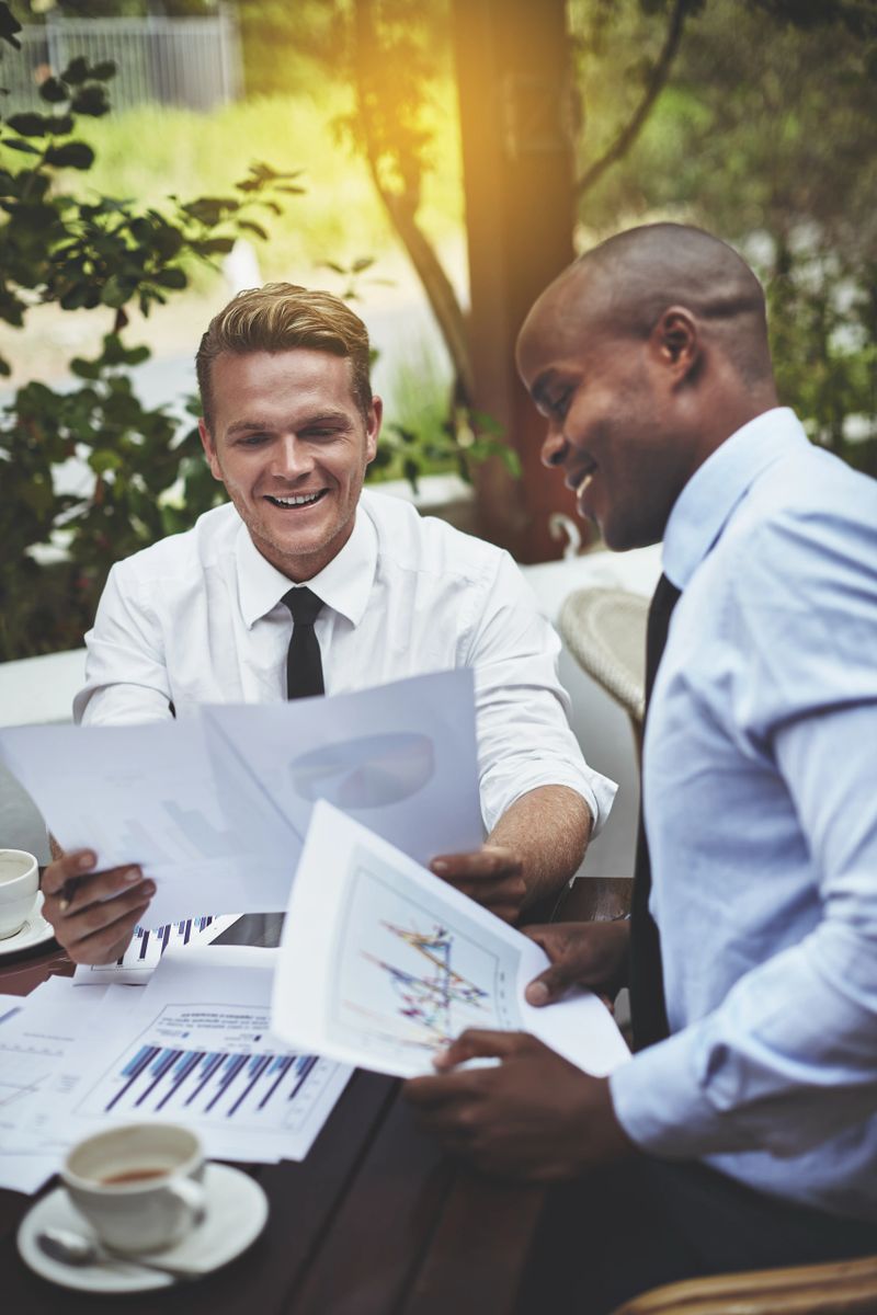 Two businessmen smile as they hold a meeting over coffee at a sidewalk cafe