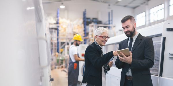Two professionals discussing work on a tablet in a factory setting.