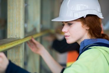 Female construction worker measuring wood with a tape measure.