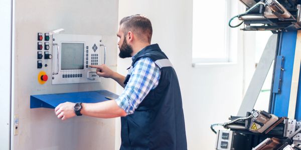 Technician operating industrial machinery control panel in a factory.