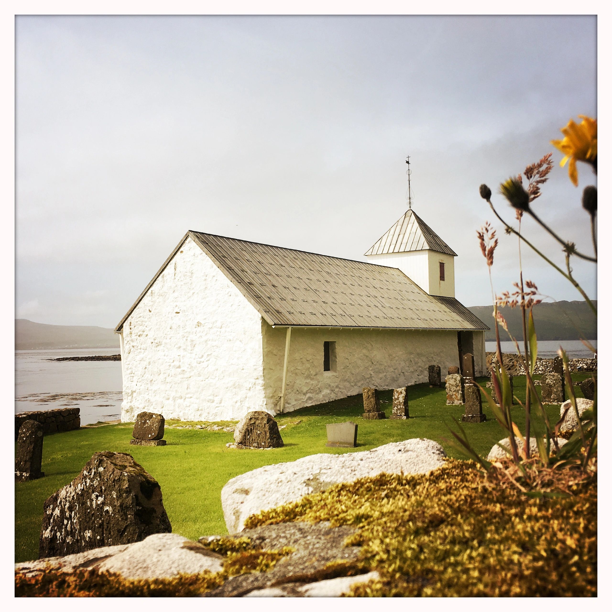 White church with a metal roof by the water and gravestones.