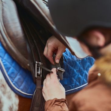 Lady tightening saddle on horse.