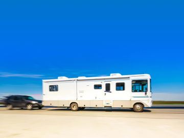 A white RV traveling on a road under a clear blue sky.