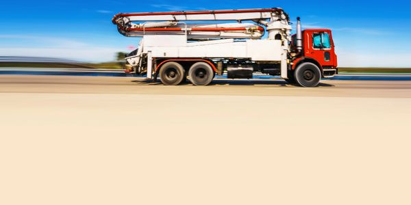 A red and white concrete pump truck speeding on a clear day.
