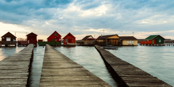 Wooden piers leading to colorful lakeside cabins under a cloudy sky.