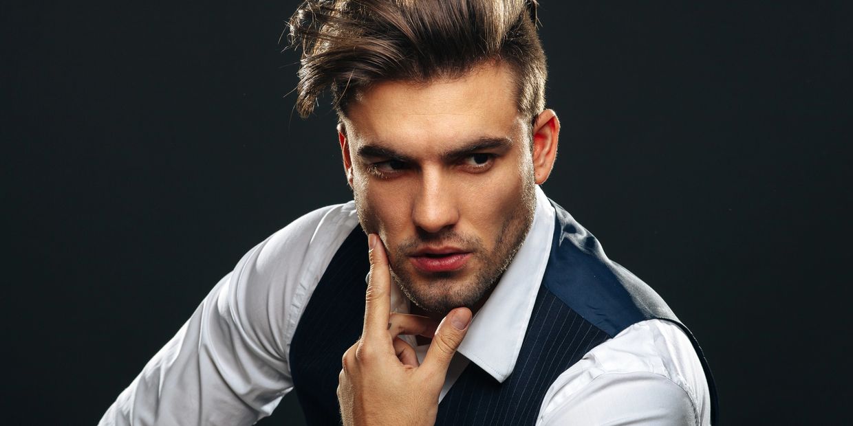 Studio portrait of a man in a white shirt and pinstripe vest with voluminous, swept-back hair,posing