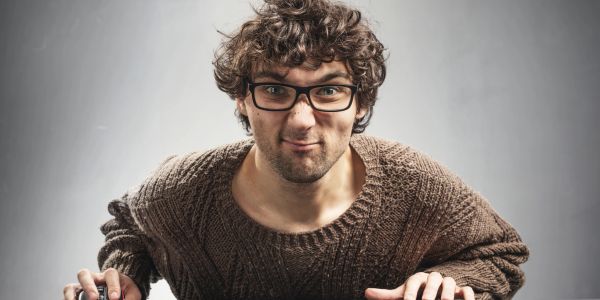 Man with curly hair and glasses wearing a brown sweater, leaning forward.