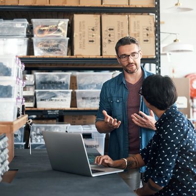 Two men discussing work in a warehouse with a laptop.
