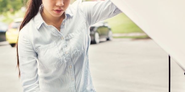 Worried woman checking under her car hood on the roadside.