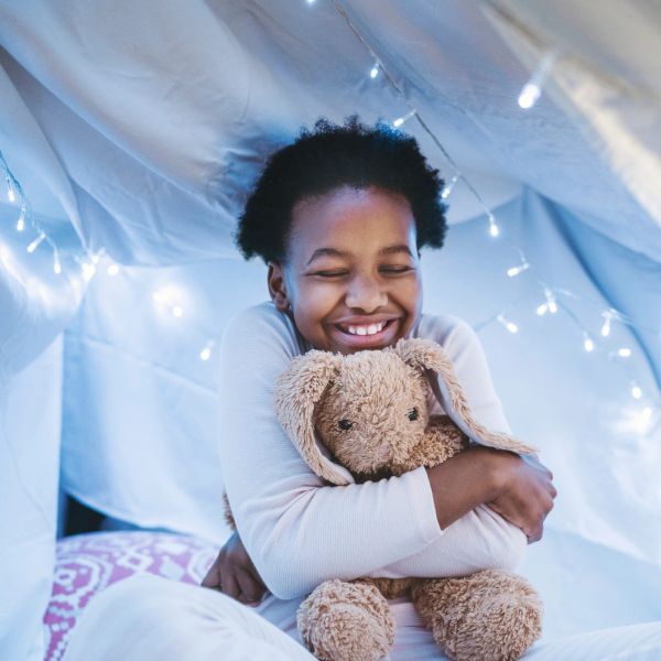 Child smiling and hugging a stuffed bunny inside a cozy tent.