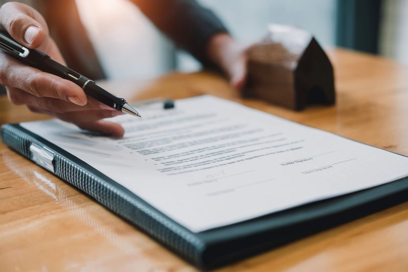 Signing contract. Close-up of confident young man signing some document while another man in shirt and tie sitting close to him and pointing document