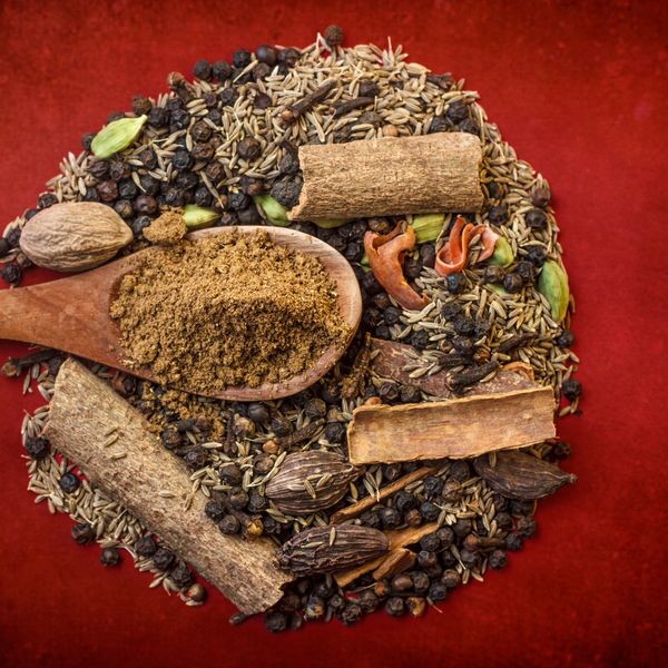 A wooden spoon with ground spice on assorted whole spices against a red background.