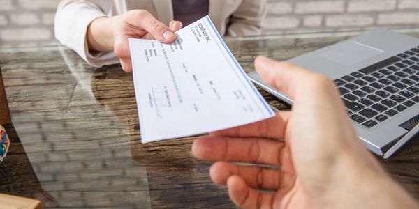 Person handing over a paycheck across a desk with a laptop.