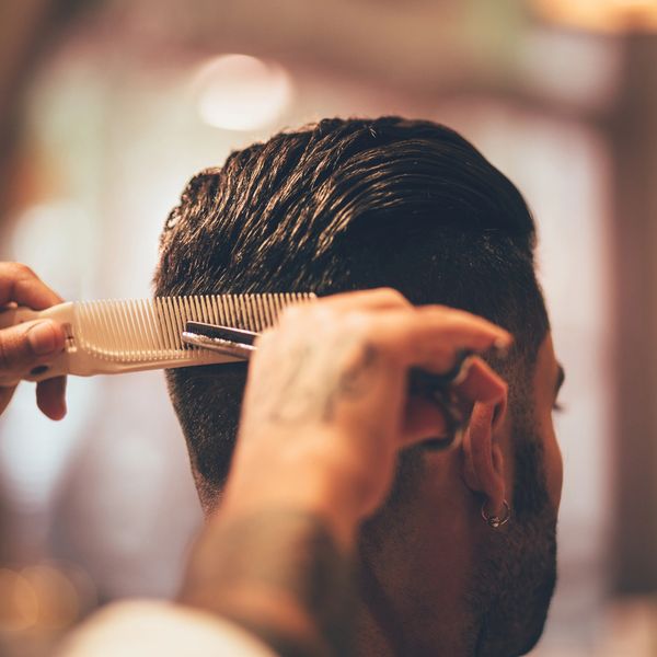 Close-up of a barber cutting a man's hair with a comb and scissors.