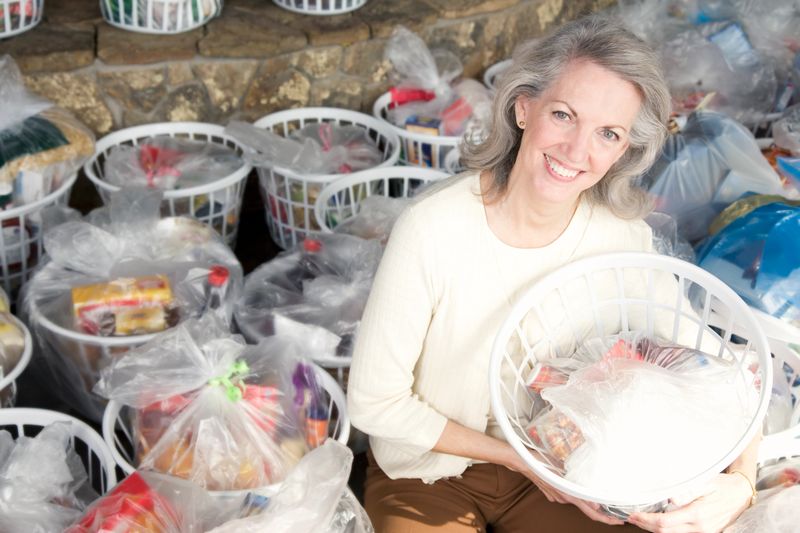 Helpful senior Caucasian woman collects food donations in baskets. She is surrounded by baskets filled with groceries.