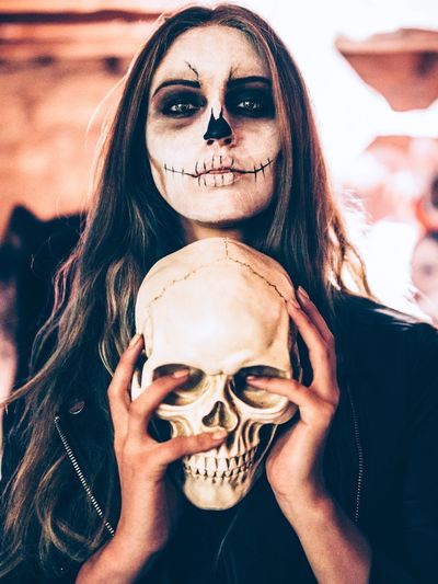 Woman with skull face paint holding a skull prop.