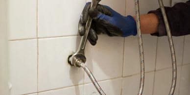A person wearing gloves tightens a plumbing fixture on a tiled wall.