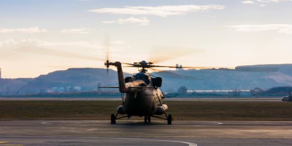 A military helicopter on a runway with spinning rotor blades at sunset.