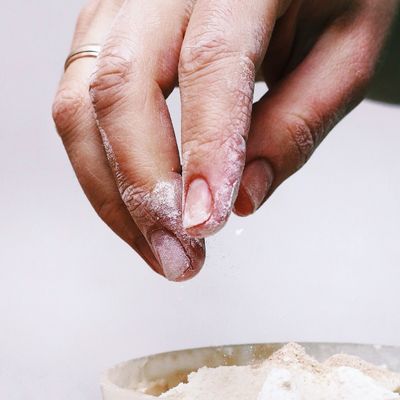 Hand sprinkling flour over a bowl, preparing for baking.