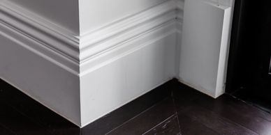 Close-up of white molding and dark wooden flooring in a corner.