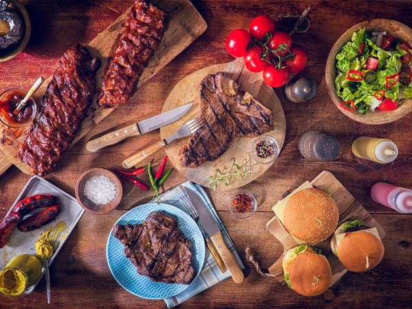 A delicious spread of grilled ribs, steaks, burgers, salad, and condiments on a rustic wooden table.
