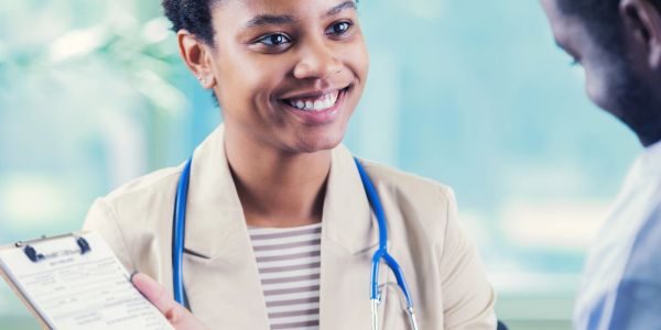 Female doctor smiling and holding a clipboard while talking to a patient.