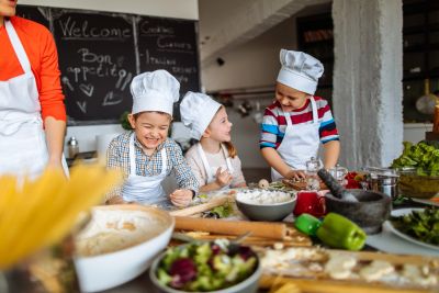 Three children in chef hats cooking happily together in a kitchen.